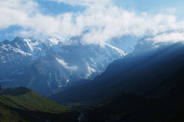 Alpine valley in the highlands with silhouettes of snow-capped mountains at dawn