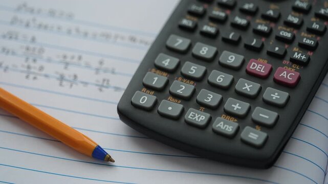 A scientific calculator and ballpoint pen lying on an open notebook with equations inside. Close up.
