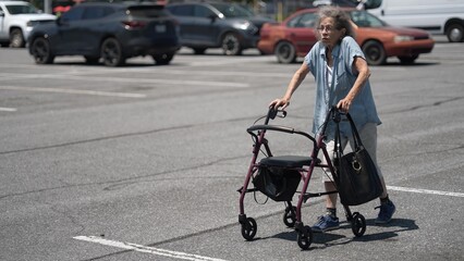An elderly woman walks cautiously with a walker in a busy parking lot, taking a moment to smoke. She is navigating her surroundings while shopping.