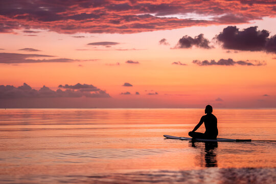 AI-generated image, Serene silhouette of a person meditating on a paddleboard during a vibrant sunset over the ocean. A peaceful yoga practice for mindfulness and tranquility.