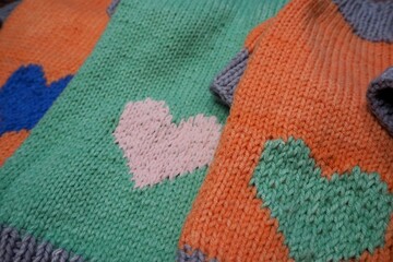 side view of knitted orange and mint dog sweaters with hearts and gray elastic of different sizes on wooden background . warm pet clothes . cozy