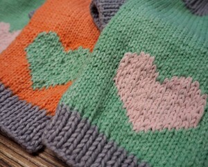 side view of knitted orange and mint dog sweaters with hearts and gray elastic of different sizes on wooden background . warm pet clothes . handmade