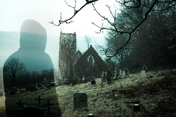 A spooky hooded figure, with a ruined church and graveyard on an eerie winters day in the countryside