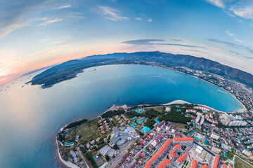 Fototapeta premium Panorama of Gelendzhik resort. Sunset. Gelendzhik Lighthouse on Kurtom Rocky Shore. Geleknji Bay and Caucasus Mountains in background. Aerial view.