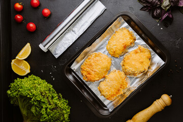 Baked chicken fillets with melted cheese on foil in a tray, top view, rustic background