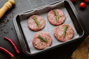 Four raw pork burger patties with rosemary ready for grilling, top view with ingredients