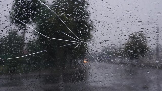 Heavy rainstorm creates poor visibility with cracked window during city drive in late afternoon