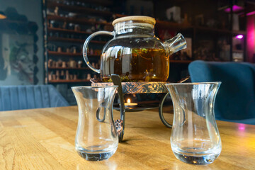 Golden hour tea ritual featuring herbal tea in a glass teapot symbolizing harmony warmth and shared moments of joy. Glass teapot with herbal tea and two glasses on a wooden table.