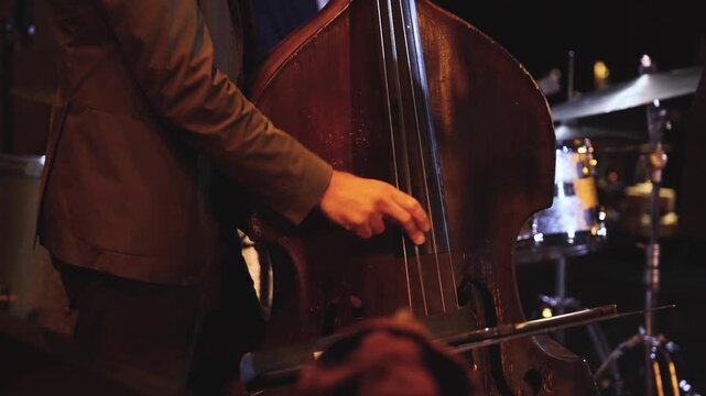 Concert view of contrabass violoncello player with vocalist and musical rock band during concert, jazz orchestra performing music, violoncellist cello jazz player on stage in a club, music arena hall