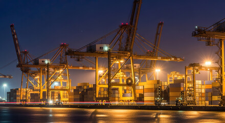 Obraz premium Nighttime Industrial Port with Massive Container Cranes and Shipping Containers