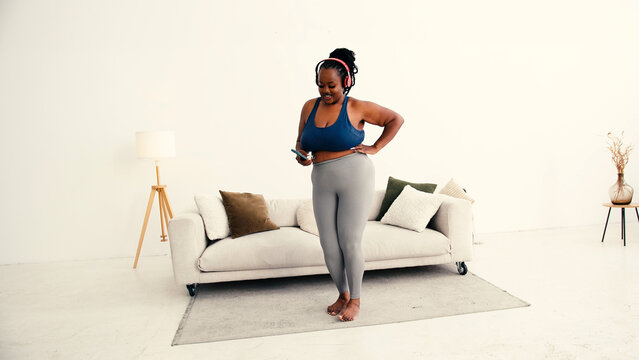 Plus size black woman dances energetically listening to music - Powered by Adobe