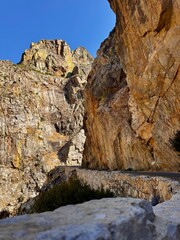 Scenic mountain road carved into massive granite cliffs under a clear blue sky in the rugged Sierra Nevada landscape.