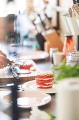 A chef is carefully slicing red tomatoes in a well-lit kitchen. The dish, a vibrant caprese salad with fresh mozzarella, sits ready to be served on a white plate