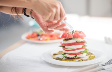 At midday, a chef meticulously seasons a Caprese salad made of tomatoes, mozzarella and basil. Olive oil and balsamic glaze glisten on a pristine white plate ready to serve