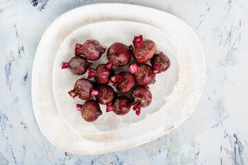 A collection of freshly harvested, small beets with dark red skin rests on a stack of white ceramic plates, ready to be transformed into a delicious culinary delight