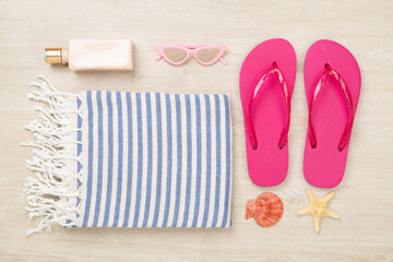 Beach towel with summer accessories on wooden background, top view