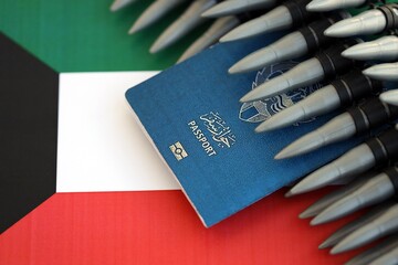 Kuwaiti passport and rifle bullets on flag. The concept of warfare and gun selling