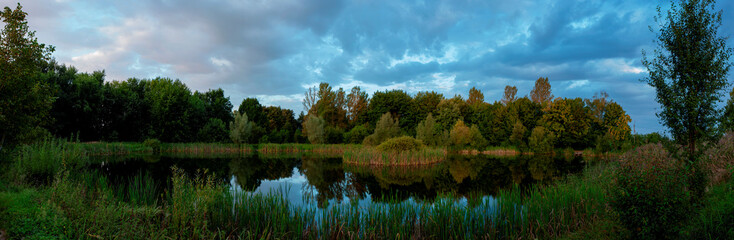 Beautiful panoramic view of the lake in the evening. Mirror reflection in the water. Panorama of a forest lake at dawn.