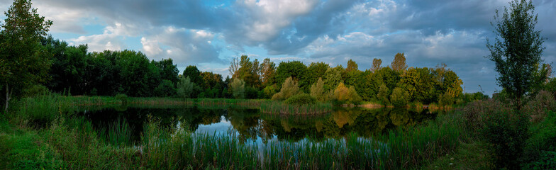 Beautiful panoramic view of the lake in the evening. Mirror reflection in the water. Panorama of a forest lake at dawn.