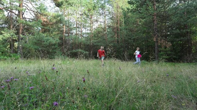 A cute boy with Down syndrome throws a frisbee with his sister in a grassy clearing in the woods. A break and fun on a family hike.
