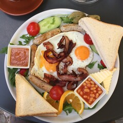 Full breakfast brunch plate with sausage, eggs, bacon, baked beans, bread and salad