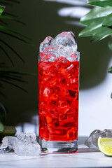 Enjoy gin tonic red cocktail drink with gin, juice, bitters, tonic water and ice. White marble table with tropical leaves in elegant lounge