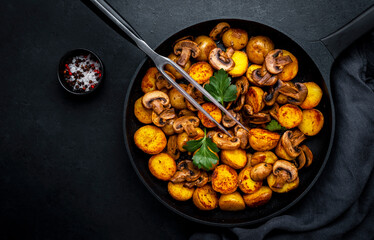 Yummy baked potatoes with mushrooms in frying pan. Black background, top view