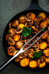 Yummy baked potatoes with mushrooms in frying pan. Black background, top view