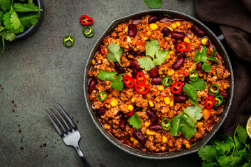 Tex-mex meet chili con carne with beef, red beans,, sweet corn, cilantro in frying pan, rusty green background top view