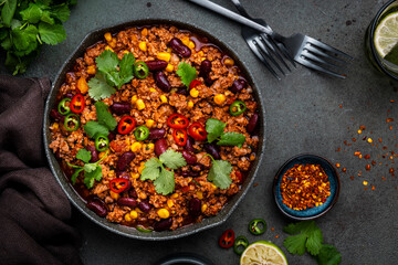 Tex-mex meet chili con carne with beef, red beans,, sweet corn, cilantro in frying pan, rusty green background top view
