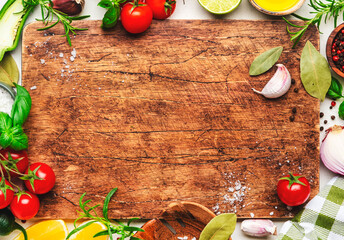 Healthy cooking food background with spices, herbs, kitchen utensils on wooden cutting board, top view. Peppercorn, garlic, basil, lemon, tomatoes and other ingredients