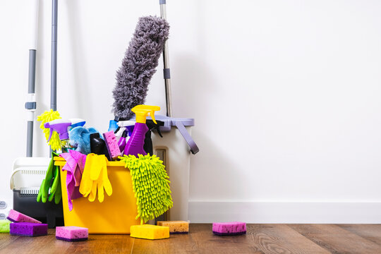 Cleaning products, household chemicals bottles and sprays, rags, sponges in orange bucket for washing the floor, brushes, broom for wiping and dusting