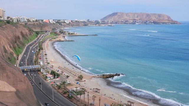 Paraglider flying over the miraflores district coastline, lima, peru, with the morro solar in the background