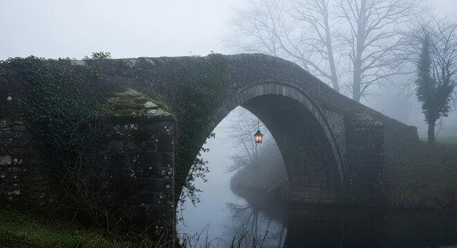 Misty morning over ancient stone bridge with lantern light