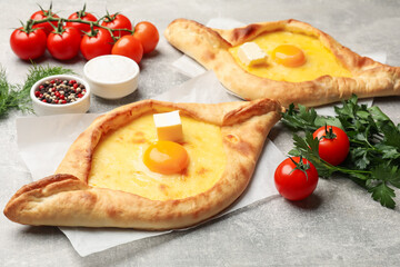 Tasty khachapuri with cheese, egg and other products on light grey background, closeup