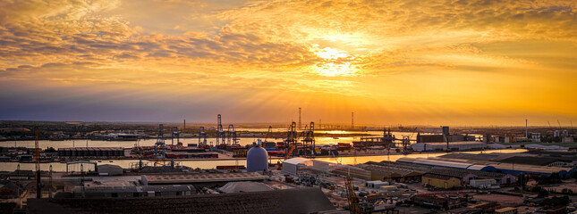 Golden hour drone shot of the busy Port of London, highlighting industrial activity, cranes, and shipping containers by the River Thames. Perfect for logistics, trade, and infrastructure visuals
