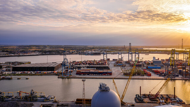 Golden hour drone shot of the busy Port of London, highlighting industrial activity, cranes, and shipping containers by the River Thames. Perfect for logistics, trade, and infrastructure visuals