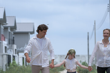 A young family walks hand in hand toward a new housing development. Seen from behind, the parents and their daughter symbolize a journey together towards a new home and a bright future.