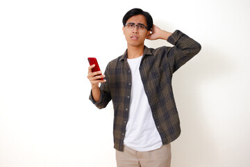 Confused young Asian man looking at his smartphone with a sad and stressed expression, isolated on a clean white background.