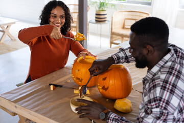 Halloween time, multiracial couple carving pumpkins at home