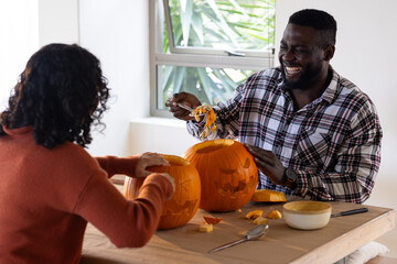 Halloween time, joyful multiracial couple carving pumpkins together at home