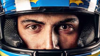Concentrated stare of male Formula one racer pilot in helmet, poised for action. Close-up of male face and eyes. Concept of motorsport, competition, readiness.
