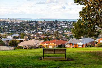 Park bench overlooking suburban houses and a wide cityscape view towards the bay in Highton,...
