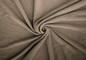 Soft fleece textile in neutral taupe beige tone, arranged in a spiral fold. Cozy fabric texture...