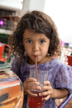 Little child girl in purple dress drinking juice at local cafe in Miami in the summer