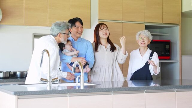 A smiling three-generation family surrounding a baby in a house