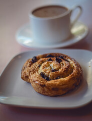 Pain aux raisins on a white plate in the foreground and coffee in the back on a blurred background