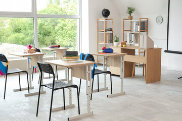 Interior of light classroom with desks, teacher's table and shelf units