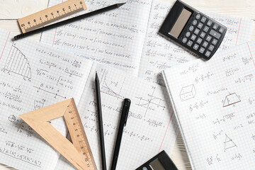 Copybooks with handwritten maths formulas, calculators and stationery on white wooden background