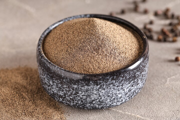Bowl with black pepper powder and peppercorns on grey background